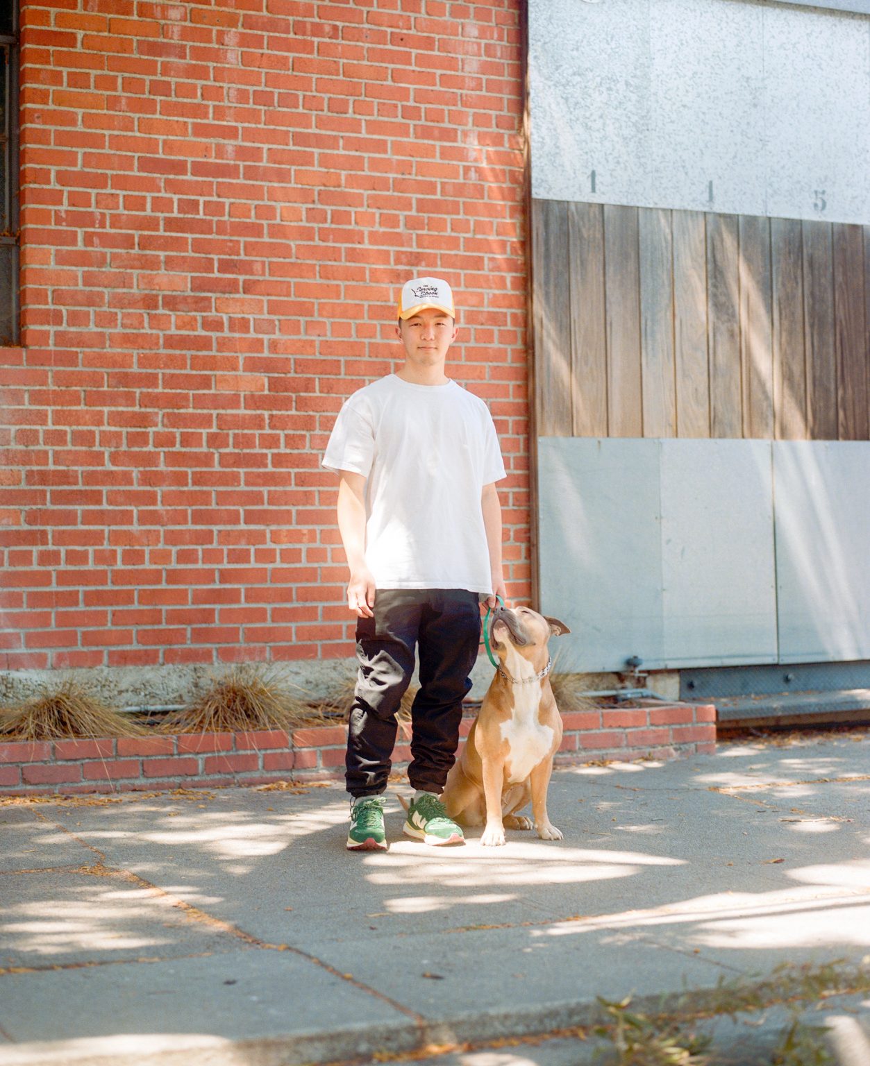 Kevin Wong standing next to his dog Chibi on a sun dappled sidewalk